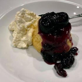 white bowl with a vanilla and cherry steamed pudding with whipped cream.